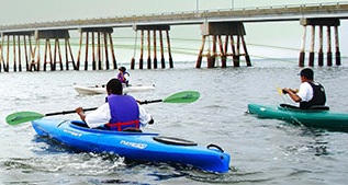 People in kayaks near a bridge.