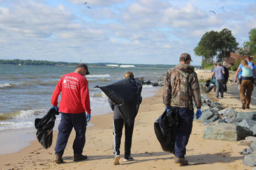 Three people walking on the beach with garbage bags picking up marine debris.