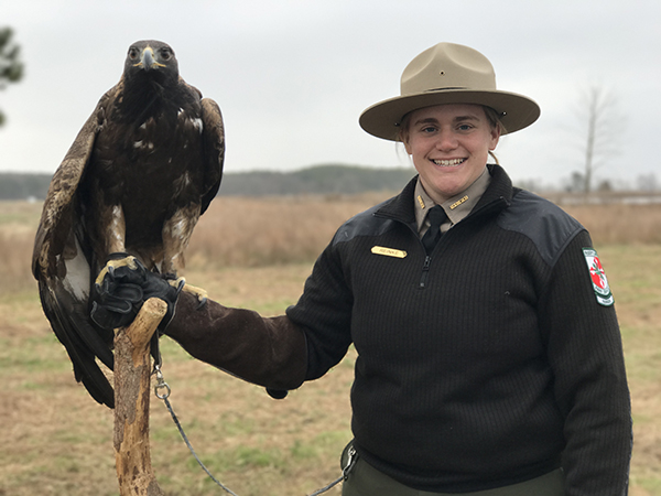 A park ranger standing outside in the winter holding a large bird on her arm.