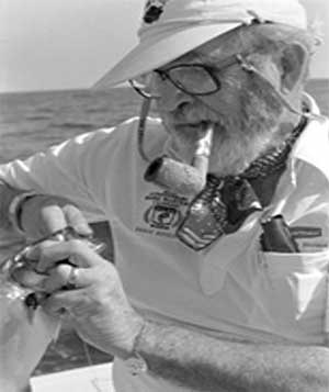 photo of Bill Burton with his signature pipe getting a fish off the hook