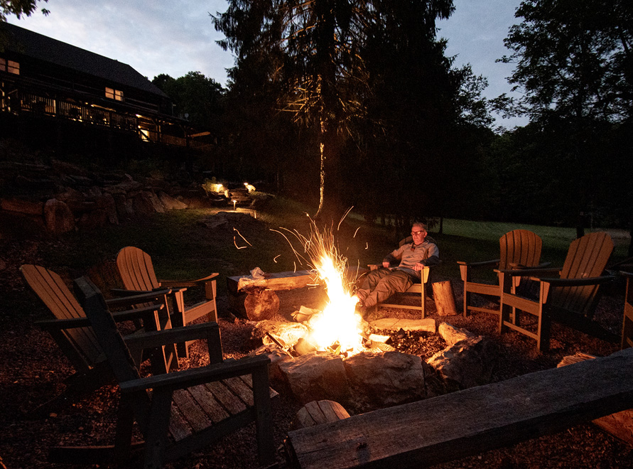 Fire in the ring behind the lodge. Large chairs and benches surround a roaring fire