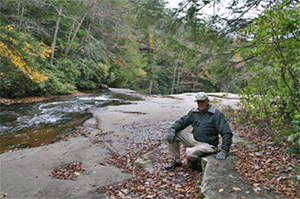 Photograph of Offutt Johnson relaxing on the Edison sitting/thinking stone in the Fall of 2012 at Swallow Falls State Park.